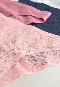 Kantstof in zachtroze met bloemenpatroon en open weving, gelaagd over marineblauw en blush textiel, met complexe ontwerpdetails.