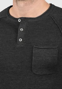 Tamno sivi dugosleeve henley majica s teksturiranom tkaninom, tri dugmeta po sredini i jednim džepom na lijejoj strani grudnog koša.