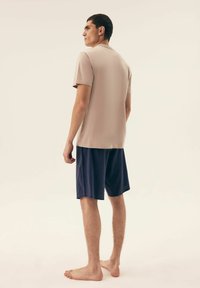 Jasno taupe krótki rękaw koszulka sparowana z granatowymi szortami z subtelnym wzorem kropek, pokazana od tyłu, z widocznymi bosymi stopami.