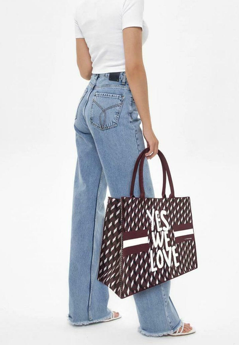 Grande borsa a tracolla in bordeaux con testo bianco "SÌ, AMIAMO." Realizzata in materiale resistente, presenta due manici superiori e una forma rettangolare.