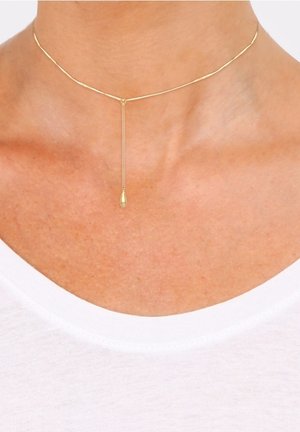 Collier ras-du-cou délicat en or avec une fine chaîne et un petit pendentif en forme de goutte suspendu au centre au-dessus d'un col de chemise blanc.