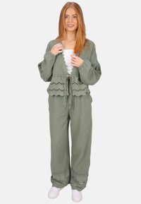 Olivgrünes Zweiteiler-Outfit bestehend aus einem strukturierten Crop-Top mit gewelltem Design und weit geschnittenen Hosen mit Spitze, kombiniert mit weißen Sneakern.