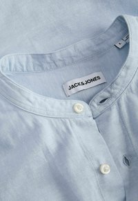Chemise en coton bleu clair avec col officier et deux boutons blancs, avec une étiquette de marque "JACK & JONES" à l'intérieur de l'encolure.