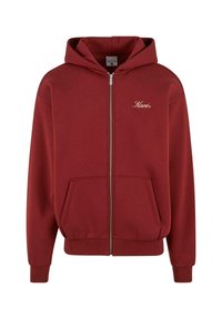 Felpa con zip color bordeaux, dotata di tasca frontale, polsini e orlo a coste. Presenta un logo dorato chiaro sul lato sinistro del petto. Tessuto morbido.