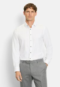 Weißes Langarm-Hemd mit Button-Down-Kragen, ausgestattet mit grauen Kn�öpfen. Kombiniert mit grauen Hosen. Glatte Textur, klassischer Schnitt.