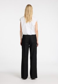 Blusa bianca a maniche corte abbinata a jeans neri a gamba larga con vita alta. I jeans presentano tasche posteriori e un taglio dritto.