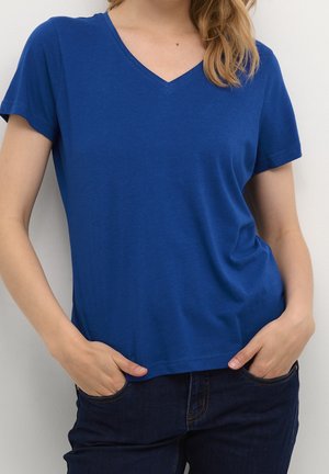 Niebieska koszulka z dekoltem w serek i krótkimi rękawami, wykonana z miękkiej tkaniny, lekko luźny krój, zestawiona z ciemnymi dżinsami. Gładka tekstura, casualowy design.