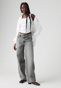 Wide-leg gray denim jeans with a faded wash, paired with a white tank top and an oversized white shirt, complemented by black pointed shoes.