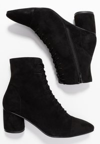 Černé semišové kotníkové boty se špičatou špičkou, zavazováním v přední části, bočním zipem a masivním podpatkem, které nabízejí hladký a texturovaný vzhled.