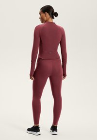 Burgundi sportos felső és leggings elasztikus anyagból. Feszes szabás, hosszú ujjak, hüvelykujjlyukakkal és varrási részletekkel. Fekete tornacipők.