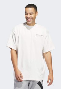 Camiseta blanca de algodón con mangas cortas, un corte holgado y un pequeño diseño impreso en el lado izquierdo del pecho. Combinada con pantalones grises con estampado.