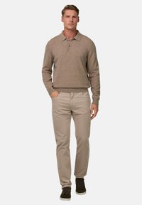 Šviesiai smėlinis megztinis su apykakle, derinamas su šviesiai smėlinėmis kelnėmis. Modelis vilki tamsiai žalius sportinius batelius, rankos kišenėse.