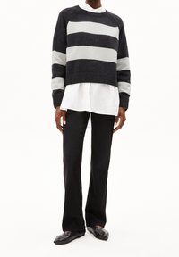 Ylimitoitettu tummanharmaa neule, jossa vaaleanharmaat vaakaraitoja, yhdistetty valkoiseen kauluspaitaan ja mustiin levenevin lahkein housuihin. Mustat tasapohjaiset kengät.