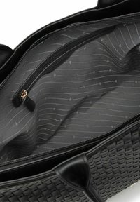 Interno di una borsa a tracolla in pelle nera intrecciata con tasca con cerniera, caratterizzato da una fodera con un motivo sottile in tonalità di nero e grigio. Superficie liscia e strutturata.