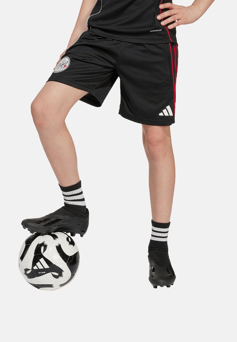 Svarta fotbollsshorts med röda ränder, ett par svarta fotbollsskor och randiga strumpor i svart och vitt. Fotbollen är vit med svarta mönster.
