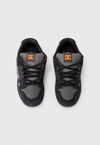 Zapatos deportivos en negro y gris con un upper de tela texturizada, lengüeta acolchada, detalles de malla y un logo en la lengüeta. Diseño con cordones.