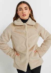 Beige faux fur frakke med en blød tekstur, krave, knapper foran og sidelommer, designet med en afslappet silhuet.