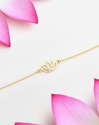 Bracciale d'oro con un design di loto al centro, con una piccola pietra preziosa come accento, su uno sfondo di petali di loto rosa.