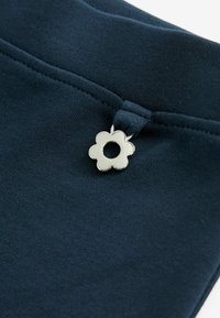 Tamnoplava tkanina s glatkom teksturom, koja sadrži srebrnu dugmad u obliku cvijeta sa središnjom rupom blizu struka.