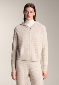 Krémově zbarvená mikina na zip s pleteným vzorem, žebrovanými manžetami a lemem, s kapucí a měkkou texturou, ve stejném designu doplněná kalhotami.