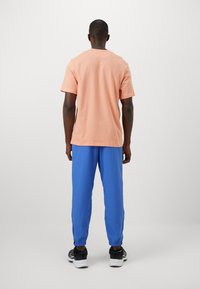 Men's outfit featuring a peach cotton t-shirt and blue sweatpants with elastic cuffs, paired with black sneakers. Simple, casual design.