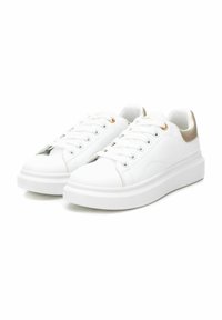 White synthetic sneakers with round toe, flat sole, gold accent on the heel, and six eyelets for laces. Smooth texture, minimalistic design.