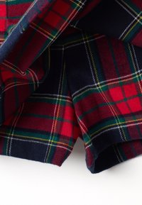 Tessuto a scacchi tartan in rosso, blu navy, verde e giallo, piegato con texture visibile e dettagli del motivo tessuto.
