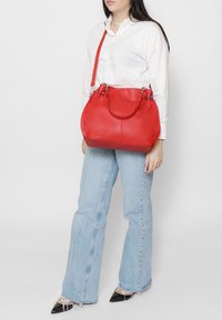 Borsa a mano in pelle rossa dalla forma arrotondata, con doppi manici superiori e tracolla regolabile. Caratterizzata da ferrature argentate e finitura testurizzata.