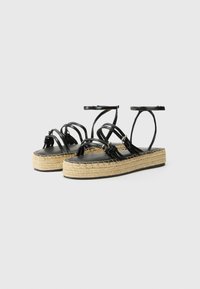 Sandalias de esparto negras de piel con suela de yute trenzado, correas al tobillo y diseño entrelazado. Plantilla plana negra con superficie texturizada.