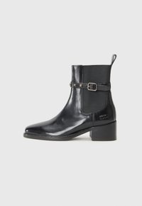 Bottine en cuir noir avec un bout pointu, des panneaux latéraux élastiques et une sangle décorative à boucle ornée de rivets. Design à talon carré.