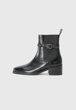 Bottine en cuir noir avec un bout pointu, des panneaux latéraux élastiques et une sangle décorative à boucle ornée de rivets. Design à talon carré.