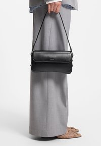 Sort læderhåndtaske med struktureret design, der vekselvirker mellem glatte og strukturerede overflader. Har en toplåse og en justerbar rem.