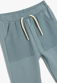 Un par de joggers en color teal con bolsillos de tela acanalada y cintura con cordón ajustable. Textura suave con un ajuste relajado y cinturilla elástica.