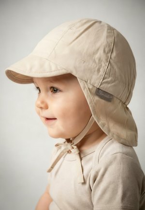 Toddler wearing a beige sun hat with neck flap and ties, smiling and facing left against a neutral background.
