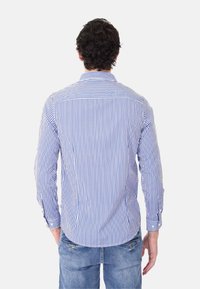 Camicia a righe da uomo con strisce verticali blu e bianche, maniche lunghe, colletto con bottoni e orlo curvo. Pantaloni in denim casual.