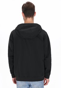 Sort hættetrøje med glat finish, elastiske manchetter og kant. Bagsiden er ensfarvet, kombineret med lyseblå jeans.