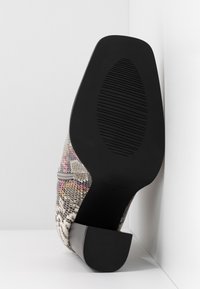Hoge hak schoen met een texturaal, meerkleurig slangenprint bovenwerk in grijstinten, roze en geel. Zwarte rubberen zool met ribbels voor extra grip.