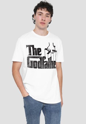 White cotton t-shirt featuring bold black text reading "The Godfather" with an illustration of hands holding marionette strings.