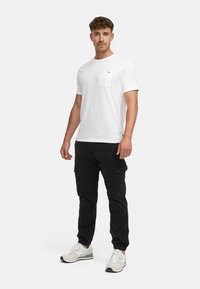 White short-sleeve t-shirt with a pocket and logo, paired with black cargo pants and light gray sneakers. Simple, casual outfit.