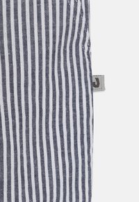 Ραφινάριστο ύφασμα σε ναυτικό μπλε και λευκό, με στενές κατακόρυφες ρίγες. Μαλακή υφή με ετικέτα ύφασματος ορατή στην πλευρά.