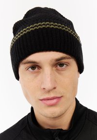 Zwarte gebreide muts met een gestructureerd patroon. Heeft een gouden streep rond de rand. Zacht materiaal, aansluitend ontwerp.