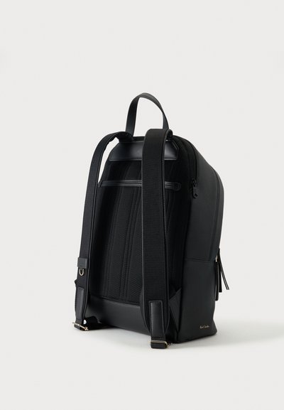 Sac à dos noir en cuir et tissu avec bretelles matelassées ajustables, poignée de transport supérieure et poche zippée latérale sur fond uni.