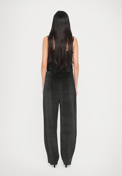 Pantalon noir, ample, en tissu texturé, avec une ceinture élastique et des poignets fuselés. Porté avec un haut sans manches.