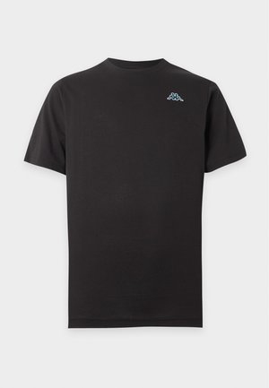 Uomo che indossa una maglietta nera tinta unita a maniche corte con un piccolo logo blu e bianco sul petto sinistro e jeans in denim azzurro chiaro.