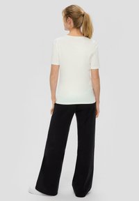 Weißes T-Shirt mit kurzen Ärmeln und Rundhalsausschnitt, kombiniert mit lockeren, schwarzen weiten Hosen. Glattes Material, lässiger Schnitt.