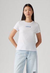 Hvit bomulls T-skjorte med korte ermer, med en blå "LEVI'S" logo på brystet. Glatt tekstur og rund halslinning.