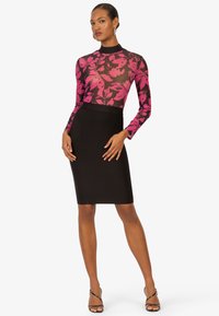 Langärmliger Bodysuit aus schwarzem Mesh mit auffälligem pinkfarbenem Blumenmuster, kombiniert mit einem figurbetonten schwarzen Bleistiftrock aus glattem Stoff.