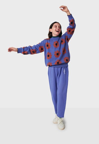 Blå sweatshirt med blommönster i orange blommor och svarta mittpunkter, ihop med ljusblå sweatpants. Vita sneakers fulländar outfiten.
