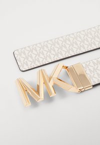 Balts jostas ģeometriskā raksta ar zelta aksesuāriem un pārspīlētu "MK" logo sprādzi, izceļot elegantu un mūsdienīgu dizainu.