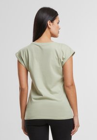 Hellgrünes Kurzarm-T-Shirt aus weichem Stoff, mit umgeschlagenen Ärmeln und lässiger Passform, getragen mit schwarzen Hosen.